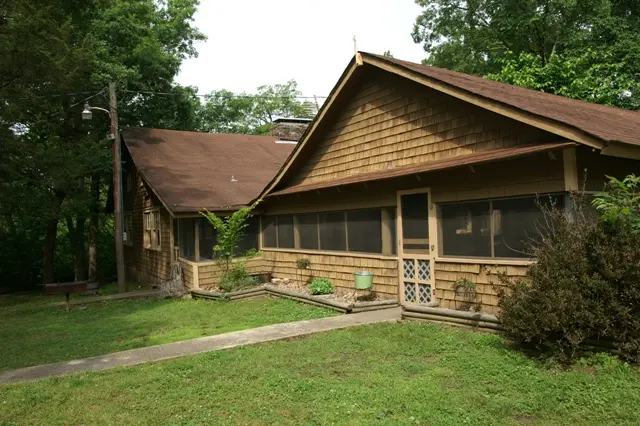 A brown house with a porch and trees in the background.