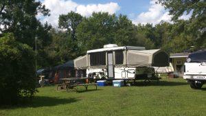 A camper trailer parked in the grass near trees.
