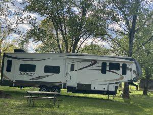 A camper trailer parked in the grass near some trees.