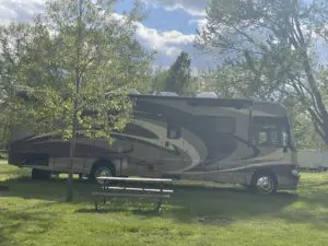 A large rv parked in the grass near some trees.