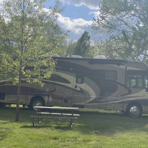 A large rv parked in the grass near some trees.