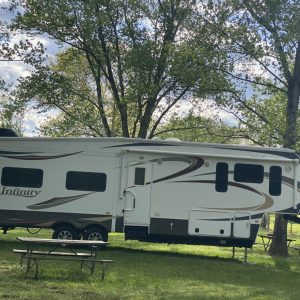 A camper trailer parked in the grass near some trees.