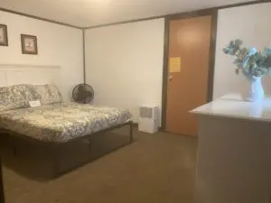 A bedroom with a bed, desk and refrigerator.