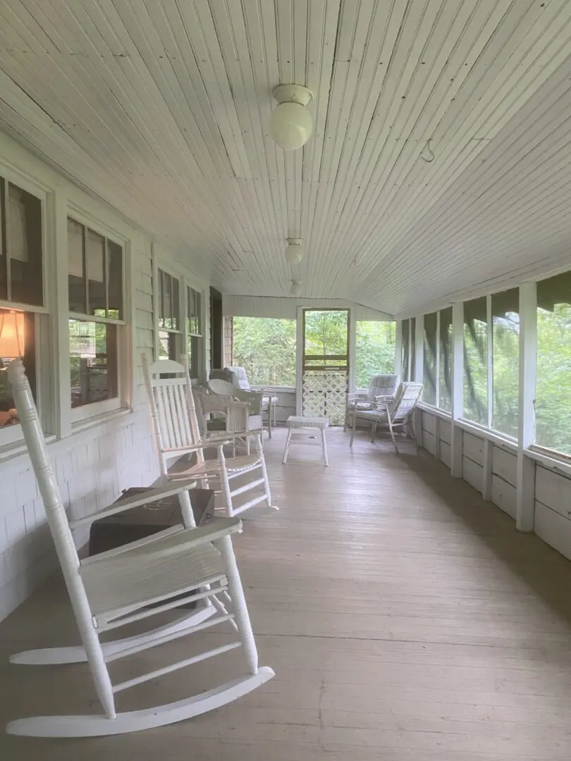 A porch with white rocking chairs and windows.